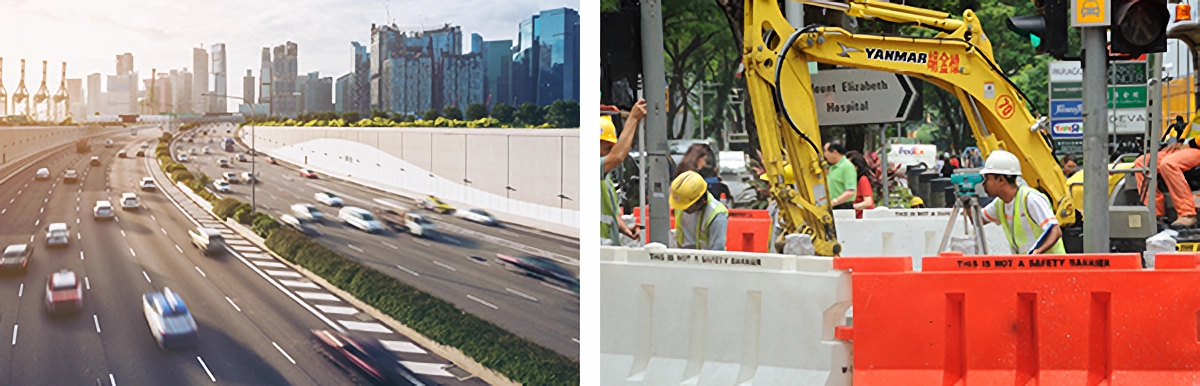 A busy highway with city skyline beside workers in hard hats operating a yellow Yanmar excavator near orange barriers.